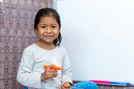 Ni&ntilde;a latina sonriente y feliz, escribiendo en la pizarra de clases con plumones de colores. Espacio para texto.