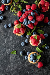Small tartlets with fresh raspberries and blueberries on a black background.