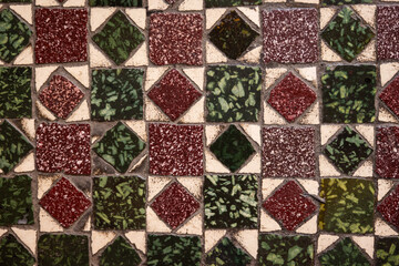 green and maroon red patterned old Italian tile with a unique pattern of squares and diamonds that is very worn from use over time in Italy Europe