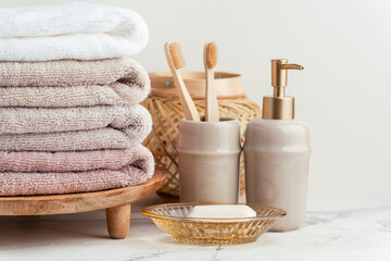 Fototapeta na wymiar Vintage golden bath supplies with stack of clean soft towels next to soap and toothbrushes. White, pink and beige towels with bathroom accessories on the white background.