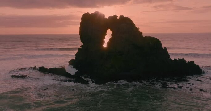 Aerial: Sun shining through hole in Giant rock at sunset, New Zealand