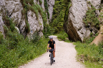 Female cyclist riding a gravel bike through rocky mountain terrain. Gravel biking adventure on beautiful mountain trails. Outdoor sport activity.Fit pretty cyclist training on nature. - obrazy, fototapety, plakaty