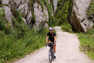 Naklejka premium Female cyclist riding a gravel bike through rocky mountain terrain. Gravel biking adventure on beautiful mountain trails. Outdoor sport activity.Fit pretty cyclist training on nature.