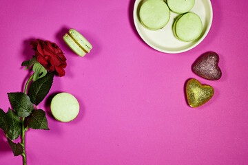 French pistachio macarons with red rose flower and  heart glitters on purple background