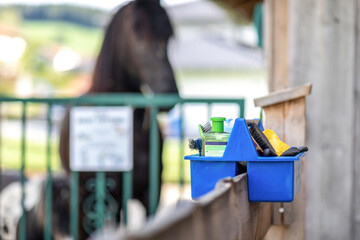 Focus on a horse groom box at a horse barn paddock in summer outdoors. A black horse is seen in the background. Text space - obrazy, fototapety, plakaty