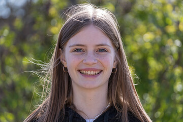 Portrait of a beautiful happy girl with blond hair and freckles looking at the camera and smiling charmingly, closeup, outdoors