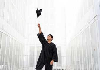 Man in graduation gown throwing mortarboard in air