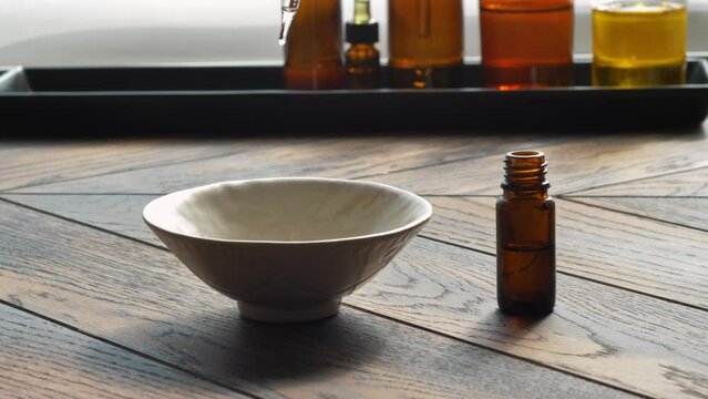 Essential oil droppind from dropper to bowl with base oil on wooden background.