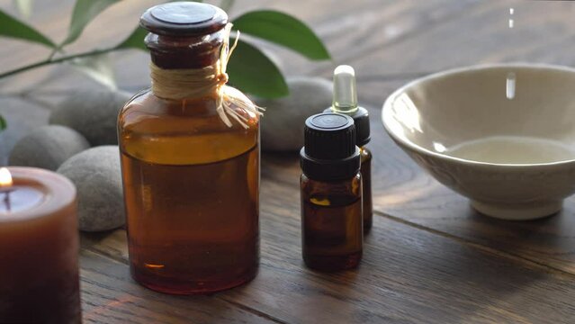 Essential oil droppind from dark glass cosmetic bottled to bowl with base oil 
