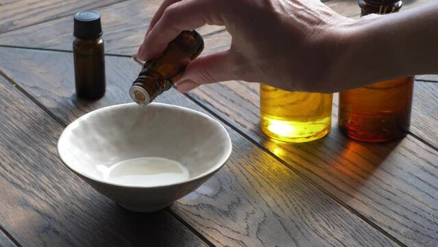 Essential oil droppind from dark glass cosmetic bottle to bowl with base oil 