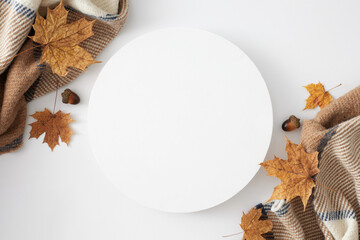 Fall's beautiful vibes. Top view shot of warm plaid, acorns, yellow autumn leaves on white background with blank circle for promo or text