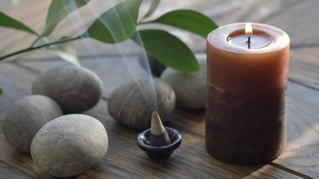 Burning incense cone with aromatic smoke, burning candel and pebble stones 