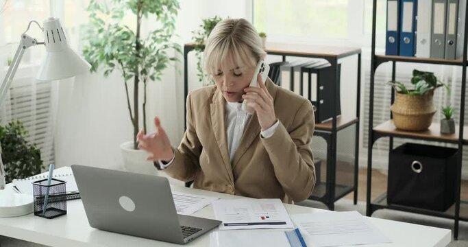 Businesswoman is shown multitasking in her office. She engages in a phone conversation while efficiently handling various work tasks. Her effectiveness and organization are evident in every move.