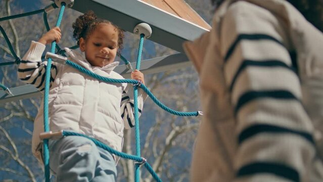 Cute child giving five to mom climbing rope ladder closeup. African girl playing