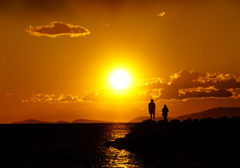 Intensive red color of sea summer sunset with silhouette of young pair looking into the sun