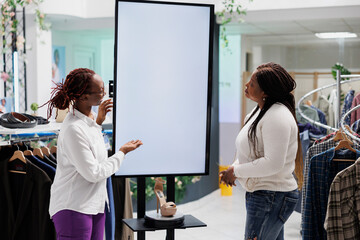 Clothing store worker helping woman to choose shoes, showing options on empty whiteboard mock up....