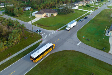 Aerial view of american yellow school bus picking up children at sidewalk bus stop for their...