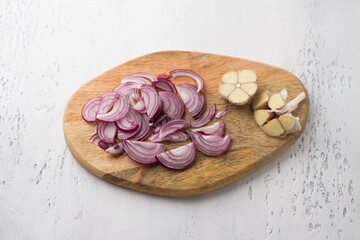 Wooden board with chopped red onion and garlic with a knife on a light gray background, top view. Cooking delicious homemade food