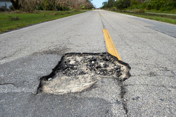 Damaged asphalt road with deep pothole on american highway surface. Ruined roadway in urgent need...