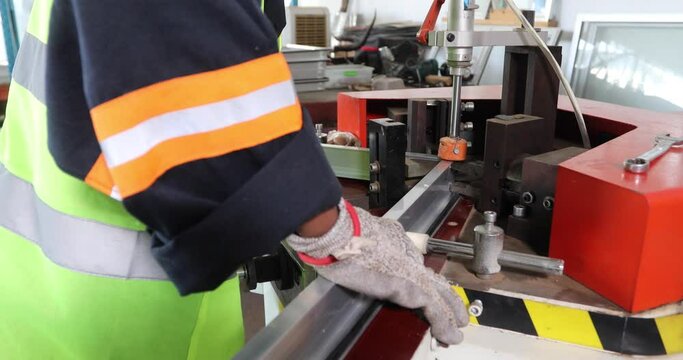 african american worker producing aluminum frames, doors and windows, in a cutting machine in a machine in the warehouse
