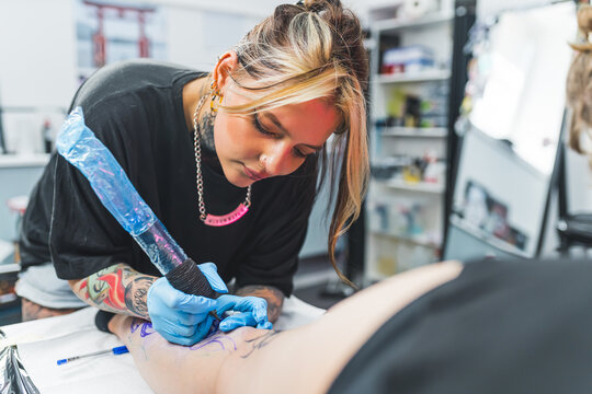 Concentration during work. Caucasian female tattooist working on her new leg tattoo design. Woman holding tattooing gun. High quality photo