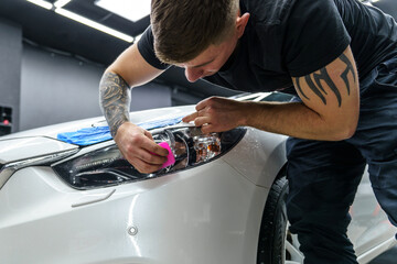 Sticker of a protective film on the headlight of a car in a car detailing studio