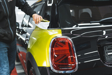car specialist cleaning a neon yellow wrap added on a black car, car detailing. High quality photo