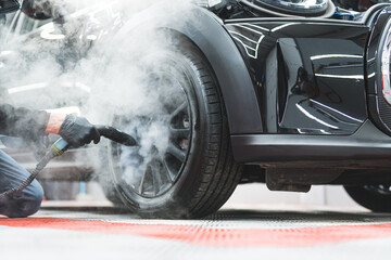 professional mechanic with black gloves cleaning a car tire with steam at the workshop. High...