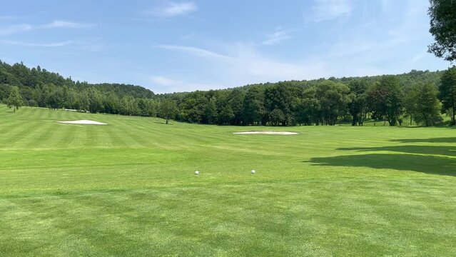 A view of a hill with a green golf course on a sunny day. Golf course with flags and sand bunkers. Green grass and trees with white sand trap.