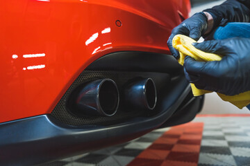 Man is wiping, cleaning and polishing with a cloth chrome exhaust pipes of modern automobile,...