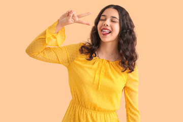 Teenage girl in yellow dress showing victory gesture on beige background