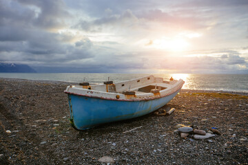 Old abandoned broken fishing boat on sea shore at sunset