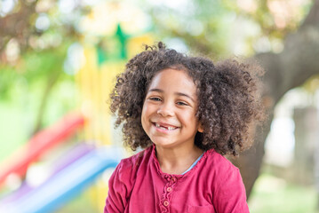 Smiling cute little african american girl with curly hair looking at camera. Portrait of happy African American girl playing in the park. - 633162429