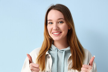 Beautiful young woman showing thumbs-up on blue background