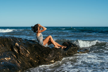 beautiful brunette girl in a silvery net stands on the stones on the seashore