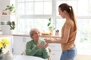 Young woman giving tasty croissants to her grandmother in kitchen