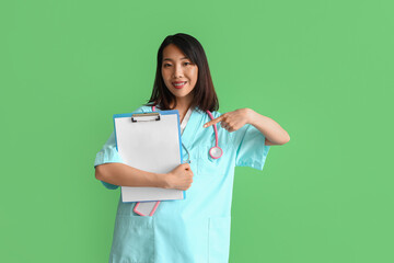 Female Asian medical intern pointing at clipboard on green background