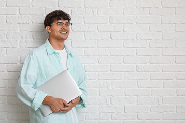Male programmer with laptop on white brick background