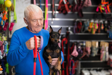 Old man choosing new collar and leash for his dog in pet shop.