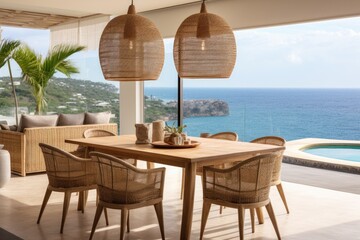 Fototapeta premium Rattan pendant lights hang above the dining table, offering a charming touch to the space and complementing the stunning ocean view.
