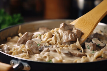 A close-up view of beef stroganoff being cooked in a pan with a wooden spoon, capturing the sizzling sound and the steam rising from the dish.