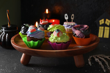 Wooden stand with delicious Halloween cupcakes on dark background, closeup