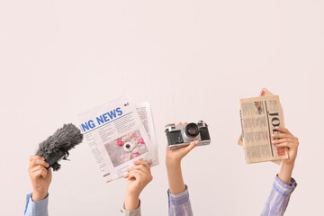 Female hands with newspapers, photo camera and microphone on light background