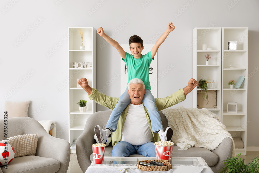 Poster happy little boy with his grandfather watching football game at home