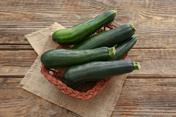 Wicker basket with fresh green zucchini on wooden background