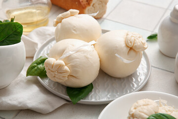 Plate of tasty Burrata cheese with basil on white tile background