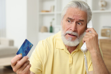 Confused senior man with credit card talking on phone at home. Be careful - fraud