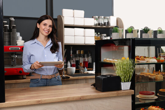 Business owner in her cafe. Woman using tablet near showcase with pastries