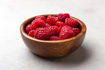 Fresh raspberries in a wooden bowl on a light grey background