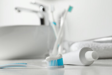 Plastic toothbrush with paste and tube on white countertop in bathroom, closeup. Space for text